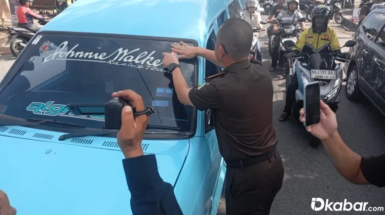 Kajari Padang, Dr Aliansyah menempelkan stiker ke kendaraan yang lewat di depan kantor Kejari Padang, Selasa (22/7/2025) (Foto:DI)